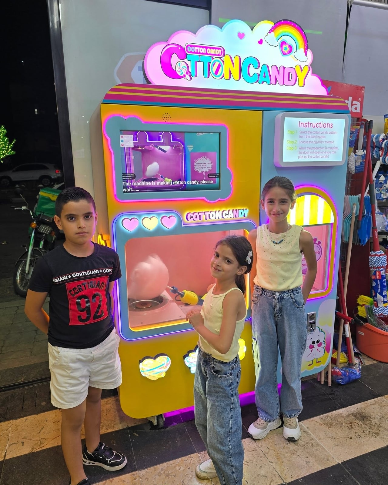 Three children beside a pink-and-yellow cotton candy vending machine.