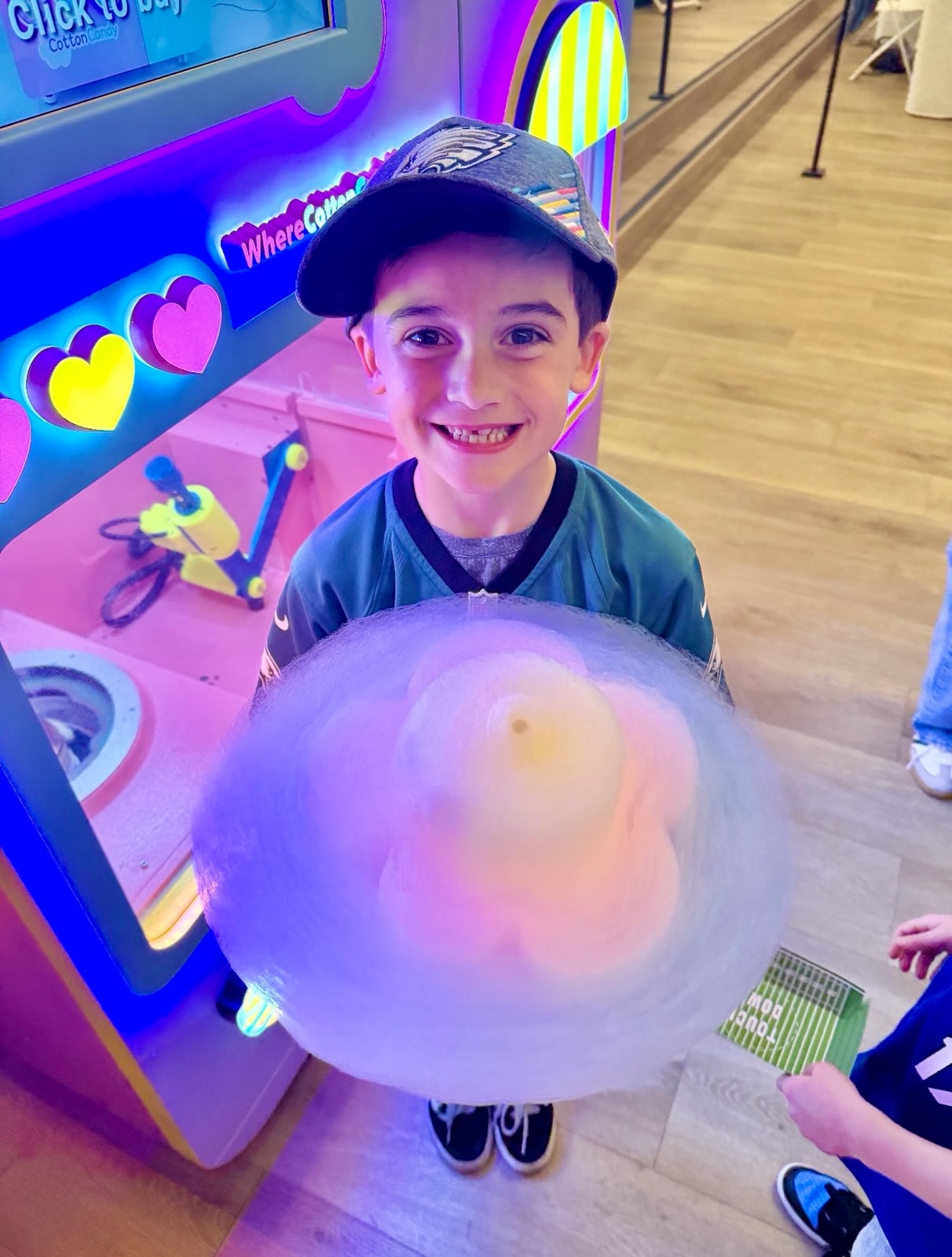 A smiling child holding a multicolored flower-shaped cotton candy beside the machine.