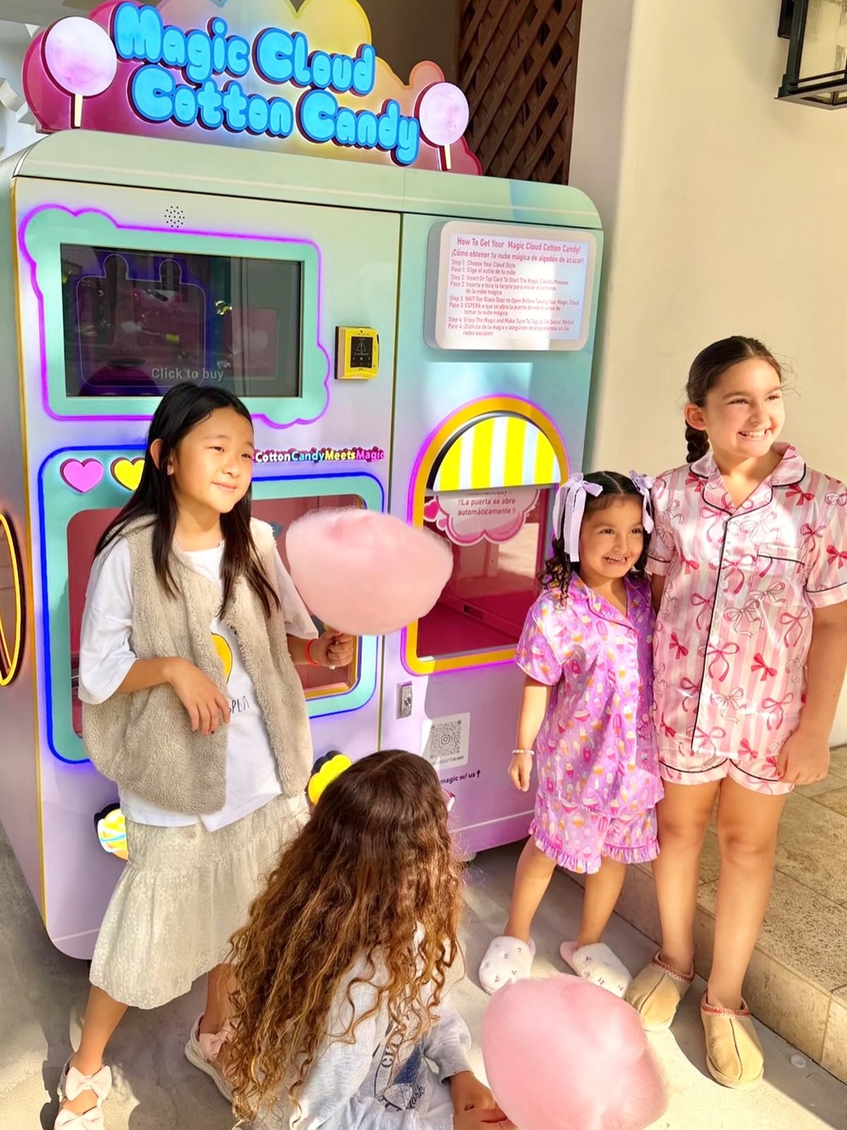 Children with cotton candy beside a pink-and-blue vending machine.