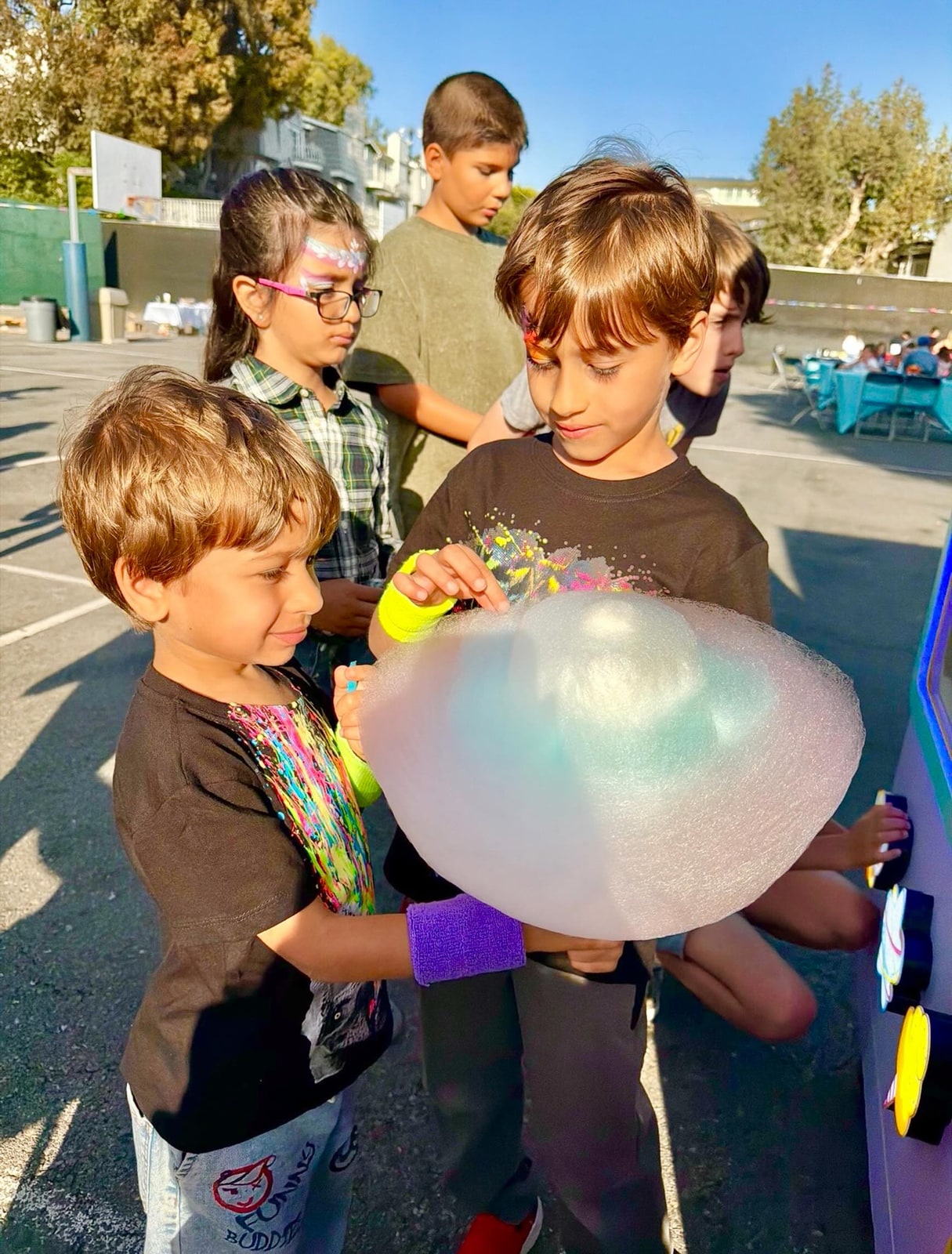 Children gathered around a large multicolored cotton candy outdoors.