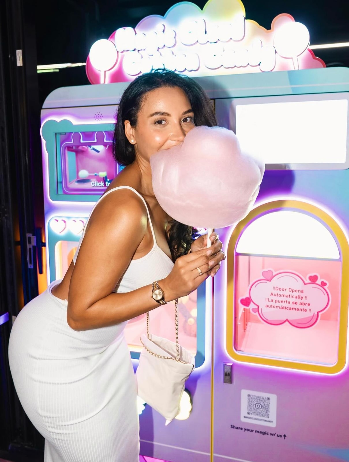 A woman holding pink cotton candy beside a pink-and-purple vending machine.